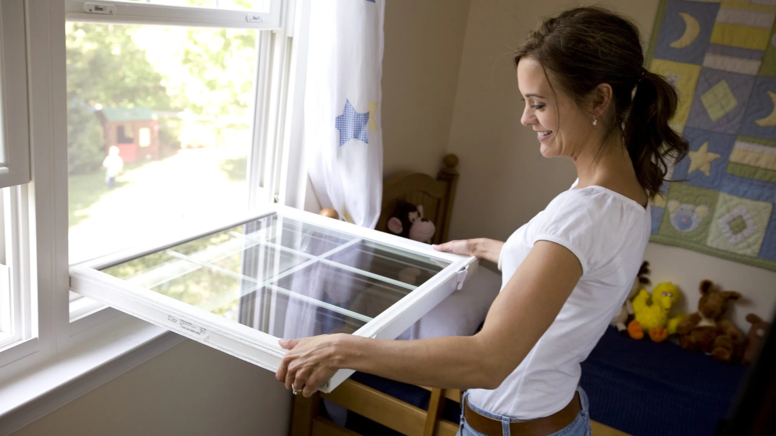 A woman opening her new double-hung replacement window next to a starry curtain